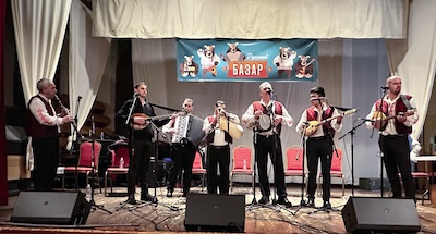 Photo of 
		7 members of Banski Starcheta standing on a stage, playing instruments and singing.